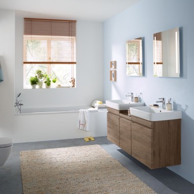 Familjebadrum med ljusblå vägg och badrumsmöbler i valnöt samt spegelskåp, spolplatta och sanitetsporslin från Geberit