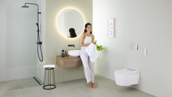 Kvinna lutar sig mot ett handfat i ett badrum med Geberit AquaClean Sela duschtoalett och Geberit VariForm tvättställ och möbler