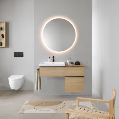 Badrum med grå väggar, badrumsmöbler från Geberit iCon i trä och en rund upplyst Geberit Option spegel