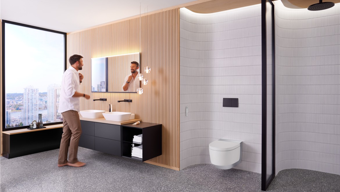 Man i ett badrum framför Geberit Option Plus Square spegel och svarta Geberit ONE badrumsmöbler (© Geberit)