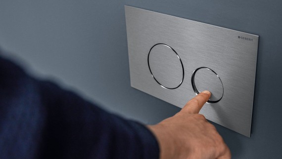 Hand aktiverar en liten spolning på Sigma40 Round spolplatta (© Geberit)